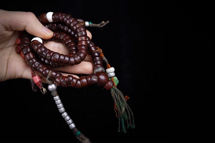 Hand holding a coiled old Bodhi seed mala with decorative beads and tassels. It symbolizes spiritual growth and meditation.