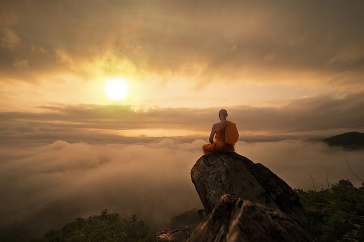 Buddhist monk meditating at sunrise on a mountaintop, symbolizing spiritual connection and transcendence.
