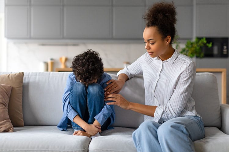 Parent gently comforting a sad child curled up on a couch - illustrating the role of patience in Buddhist parenting.