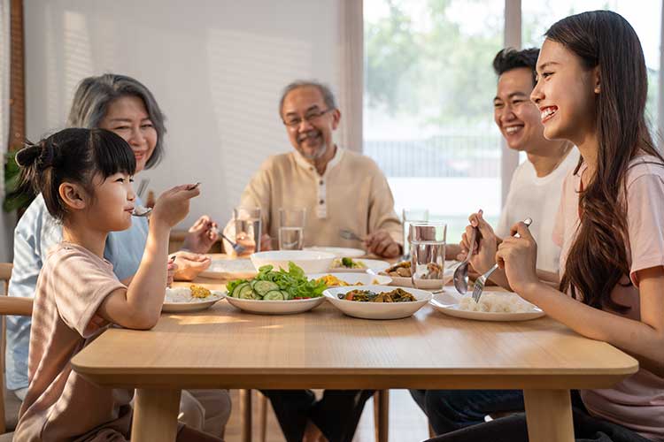 Smiling multigenerational family enjoying a meal together, illustrating everyday Buddhist parenting practices like gratitude, presence, and togetherness.