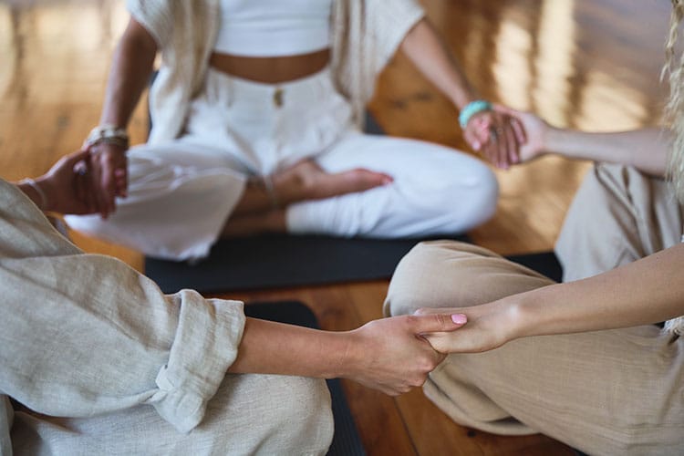 A circle of people sitting in a support group and holding hands.