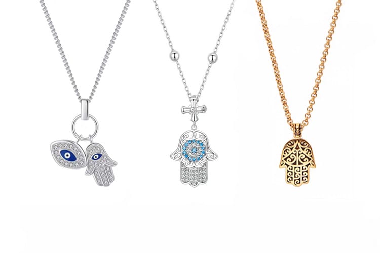Three Hamsa necklaces displayed side by side: one silver with an evil eye charm, one ornate with blue stones, and one gold with intricate filigree. The image highlights the variety of materials, colors, and symbolic details in Hamsa pendant designs.