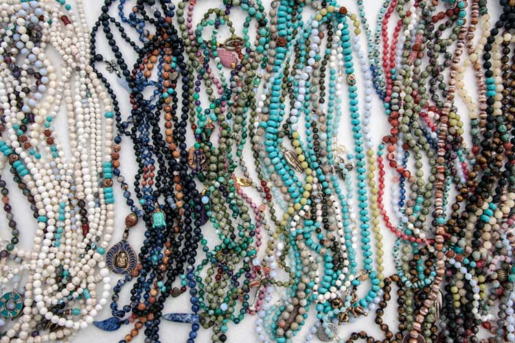 Variety of colorful gemstone mala beads laid out, featuring stones like Labradorite, Rose Quartz, and Turquoise - each symbolizing different energies and intentions for meditation and healing.