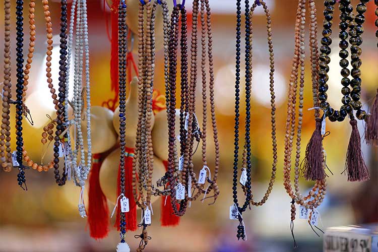 Various strands of mala beads in different styles and colors hanging at a market, symbolizing the importance of selecting mindfulness tools with intention and care.
