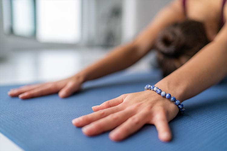 Close-up of a person in a yoga pose wearing a blue gemstone mala bracelet, symbolizing a portable and meaningful option for meditation and mindfulness on the go.
