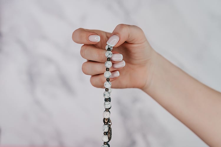 Close-up of a hand gently holding a white stone mala. It focuses on the larger guru bead that symbolizes spiritual guidance and the starting point of meditation practice.