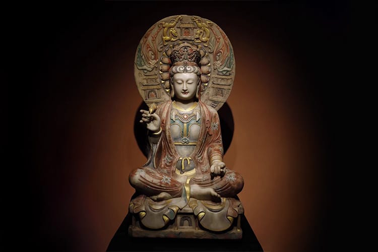 Ornate Kuan Yin statue seated in a meditative posture with one hand raised in a symbolic gesture.