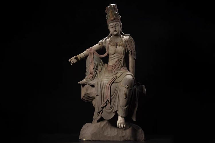Wooden statue of Kuan Yin seated in the royal ease position. It expresses the Kuan Yin statue meaning through her relaxed form and gentle gaze.