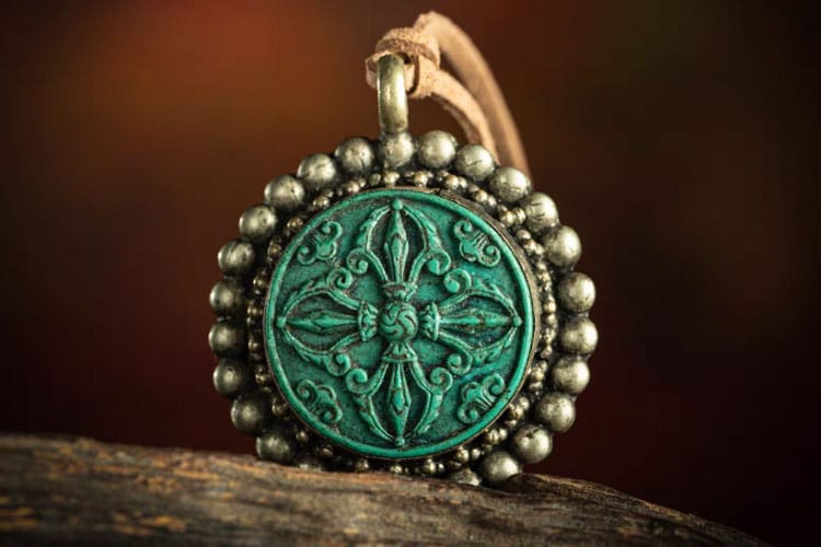 A round Tibetan pendant with an ornate turquoise vajra design. It is framed by silver beads and hanging from a leather cord, representing sacred symbolism and meditation in Tibetan Buddhist art.