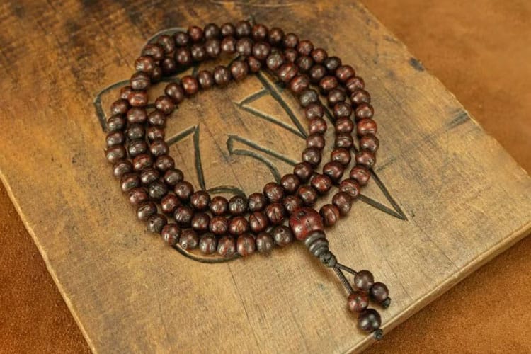 A 108-bead Bodhi seed mala with a guru bead and tassel, coiled on a carved wooden board.