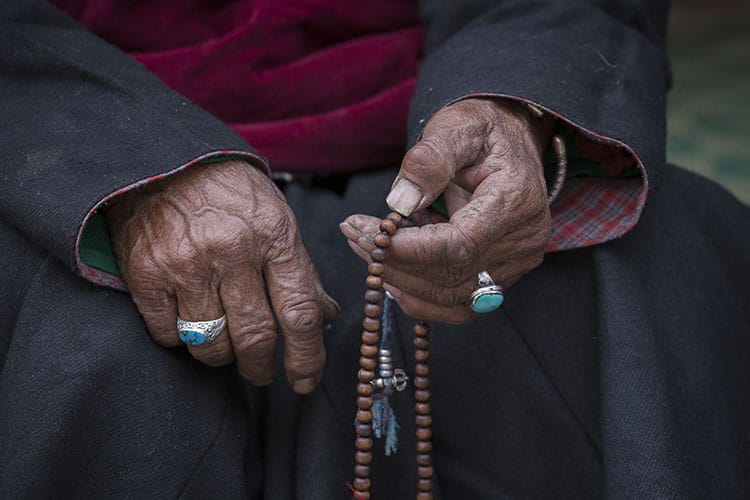 Elderly hands holding a strand of mala beads, symbolizing a deep connection to spiritual tradition and centuries-old meditation practices.