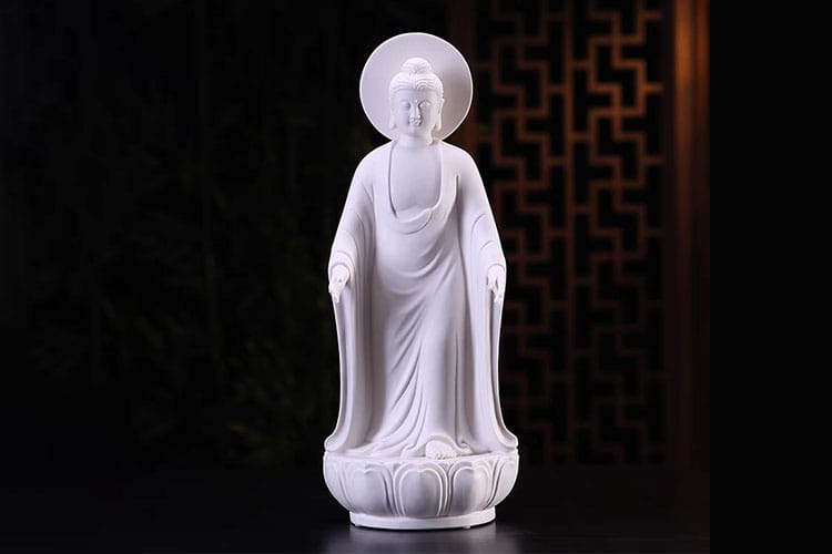 A luminous white Buddha statue stands gracefully atop a lotus pedestal, elevated and centered against a dark, patterned background.