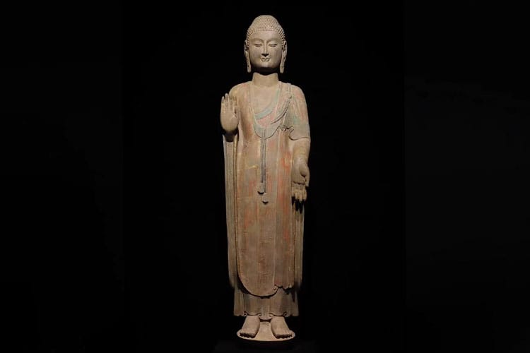 An ancient Buddha statue in a standing posture with hands held in symbolic gestures.