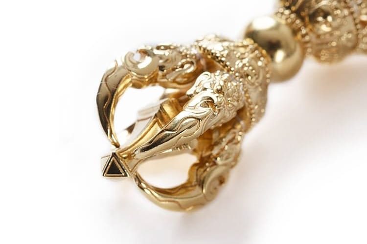 A close-up of an intricately detailed golden Vajra, showcasing ornate carvings and symmetrical prongs. The design symbolizes spiritual power, inner clarity, and protection from both external and internal negativity.