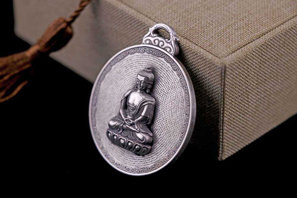 A silver medallion depicting The Buddha with the Surangama sutra encicling him