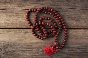 A Bodhi seed mala with a red tassel resting on a rustic wooden surface, symbolizing the journey of inner awakening, resilience, and spiritual growth.
