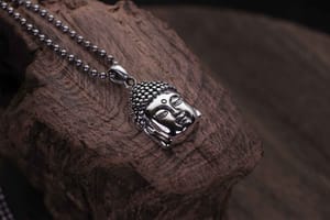 A silver Buddha head pendant on a block of wood.