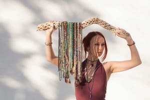 A woman holding a piece of driftwood draped with many colorful mala bead strands, symbolizing the variety and personal connection one can find when choosing mindfulness beads.