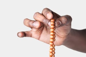 A close-up of a hand slowly moving through a strand of light wooden mala beads.