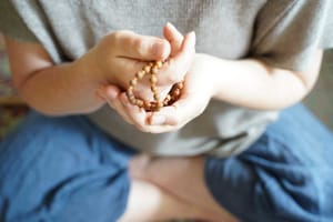 Close-up of a person seated cross-legged, gently cupping a wooden mala in their hands. It symbolizes mindfulness, prayer, and the sacred journey of spiritual connection.