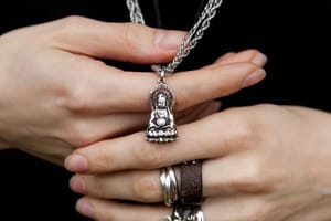 Close-up of hands holding a silver Buddhist pendant shaped like a serene, seated figure.