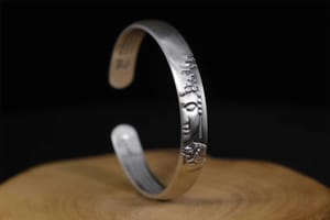 A handcrafted silver bracelet featuring a serene Buddha face and lotus flower design. It symbolizes mindfulness, compassion, and the enduring legacy of Buddhist jewelry.