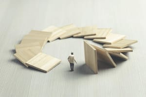A man stands at the center of a circular domino effect, symbolizing how actions set in motion eventually return. This illustrates the karmic cycle of cause and effect.