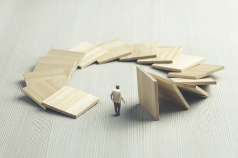 A man stands at the center of a circular domino effect, symbolizing how actions set in motion eventually return. This illustrates the karmic cycle of cause and effect.